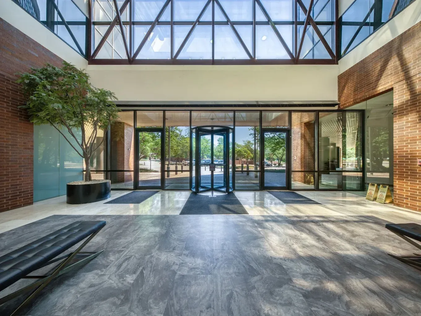Modern glass atrium with brick walls, large windows, and sunlight casting long shadows on the floor