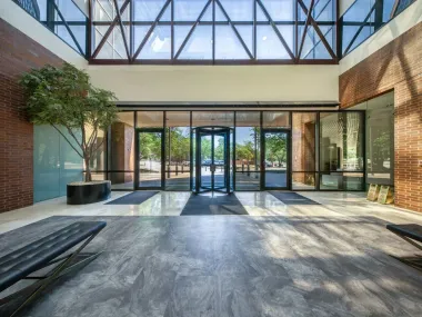 Modern glass atrium with brick walls, large windows, and sunlight casting long shadows on the floor