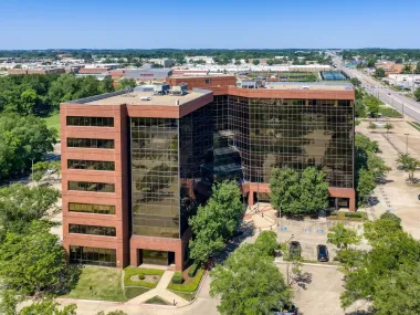 A red-brick office building with glass facades surrounded by trees in an urban area.