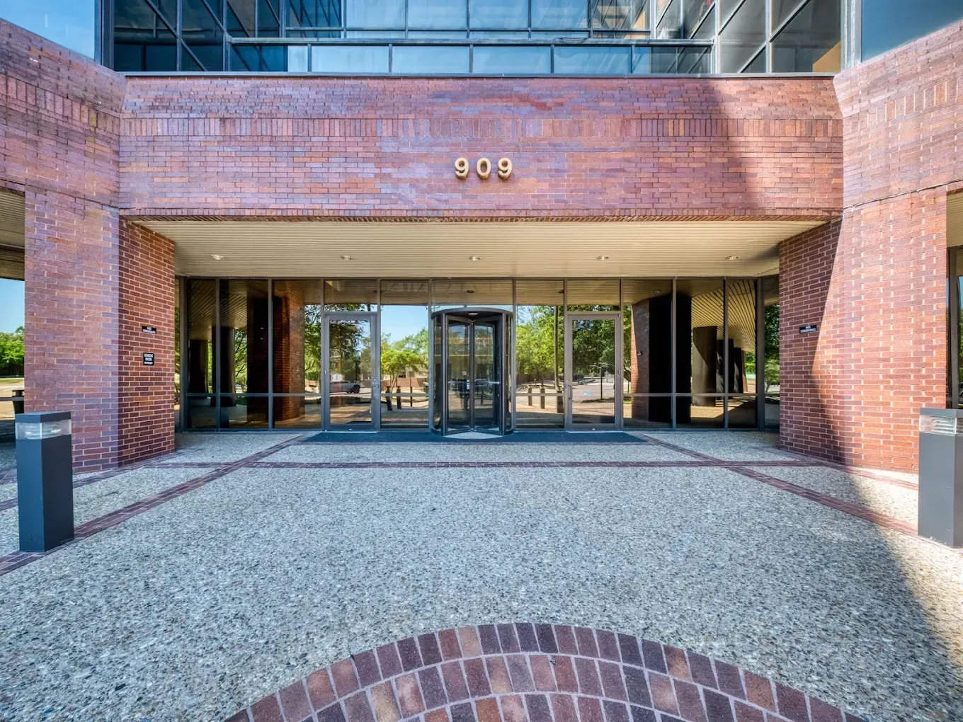 Brick building entrance with glass doors, brick archway, and gravel forecourt.