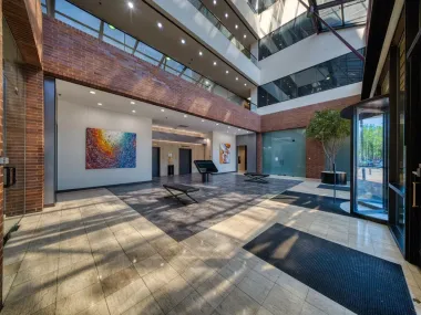 Modern atrium with brick walls, glass railings, skylights, and colorful wall art in a bright lobby