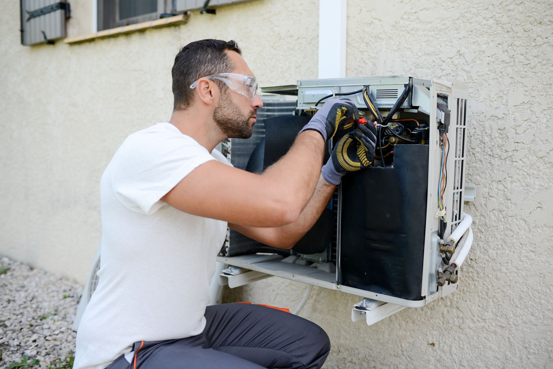 A man is working on an air conditioner outside of a building.