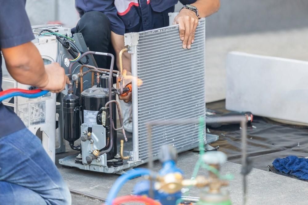 Two men are working on an air conditioner on the ground.