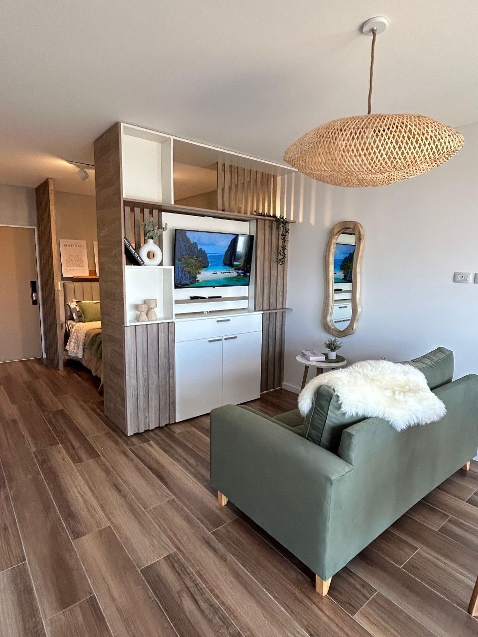 Moderno apartamento tipo estudio con sofá verde oliva, televisión y suelo de madera.
