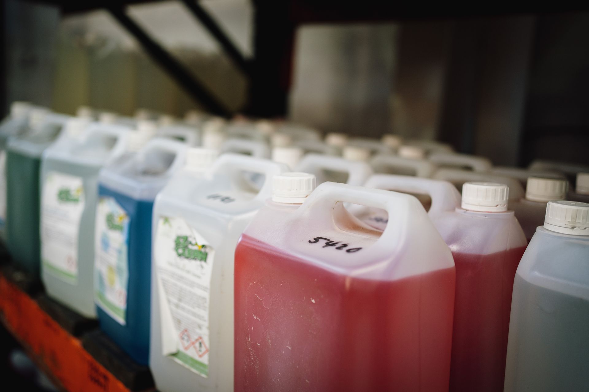 A row of cleaning supplies are lined up on a shelf in a warehouse.