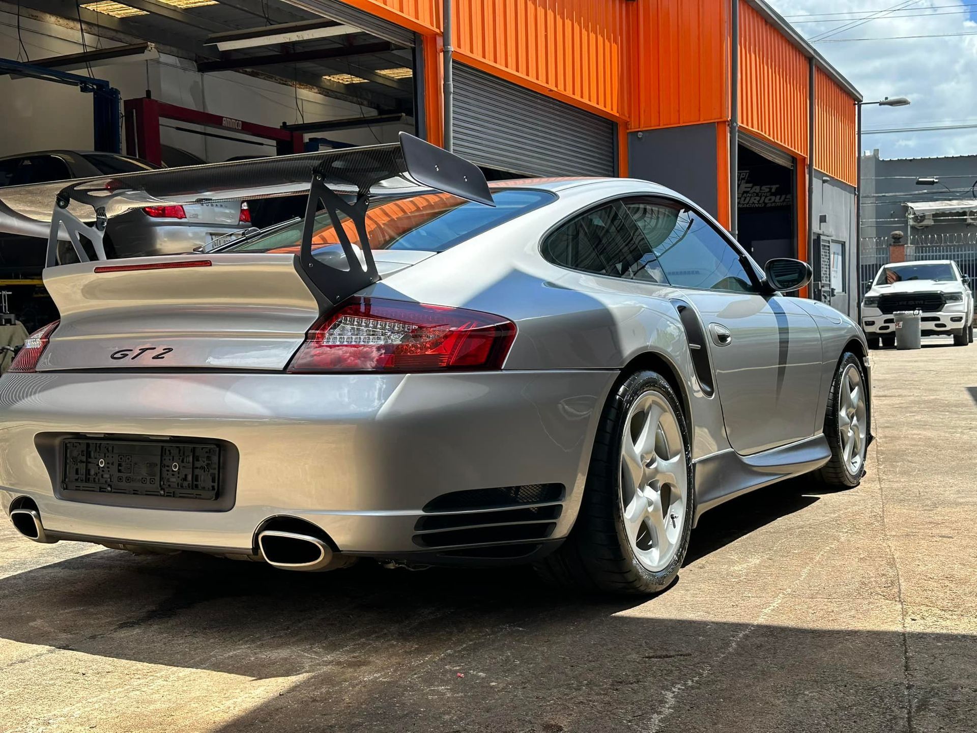 Silver Porsche 911 GT2 parked outside a garage. Features large rear wing and wide tires.