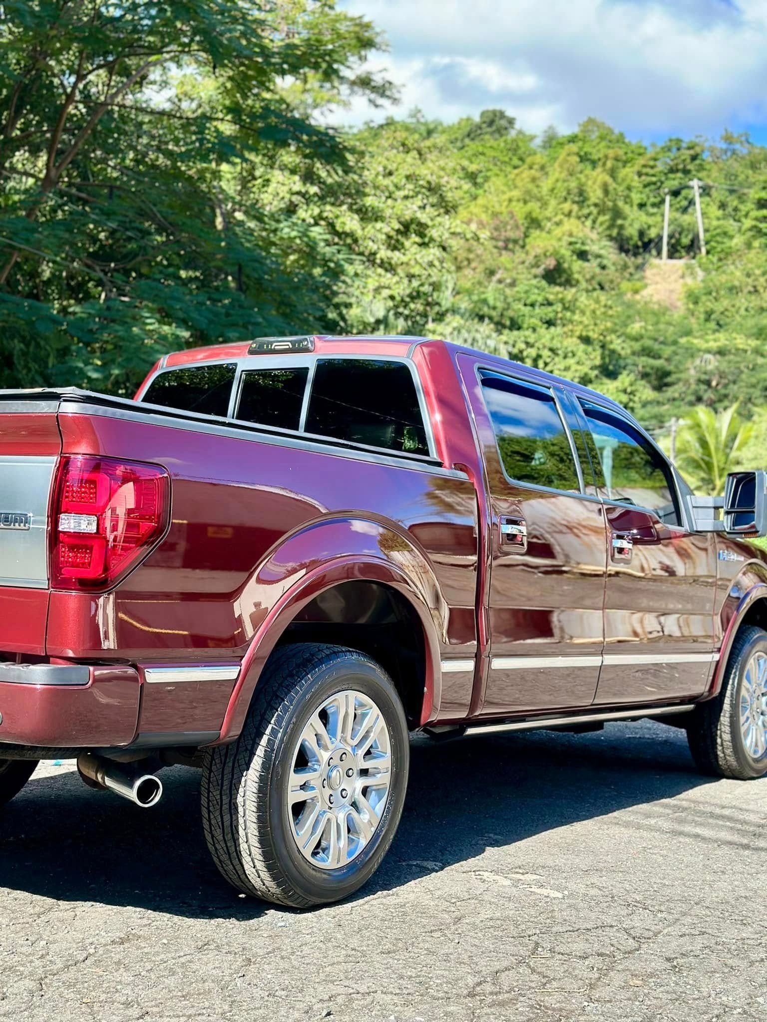 Burgundy pickup truck parked outdoors with a green hillside in the background.