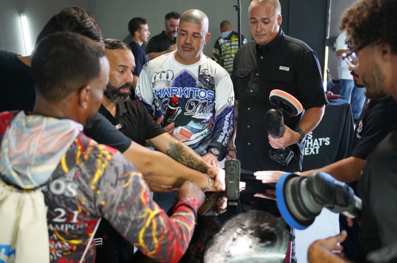 Person wiping a dark car with a yellow microfiber cloth.