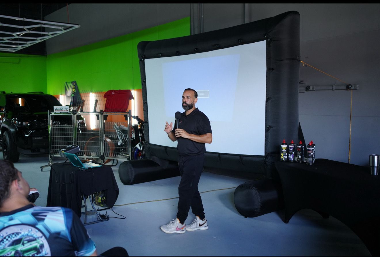 Man demonstrating detailing products to an audience in a workshop setting.