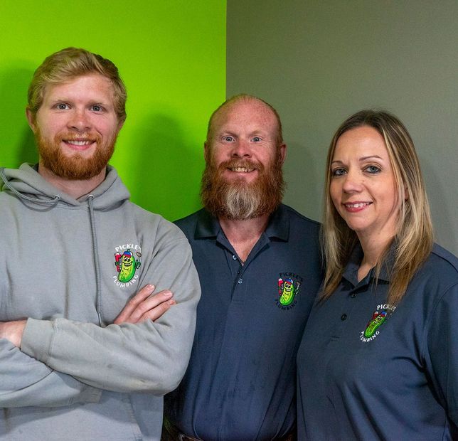 Three people are posing for a picture in front of a green wall.