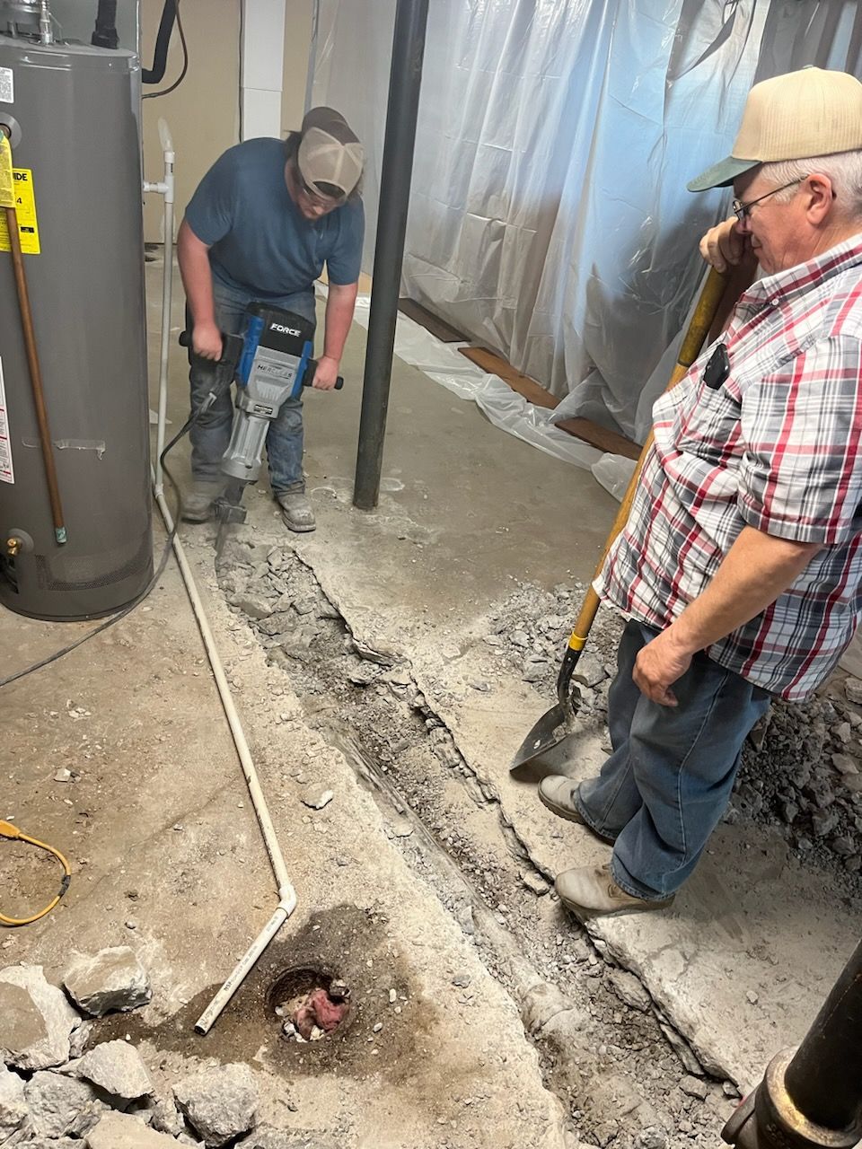 Two men are working on a concrete floor in a basement.
