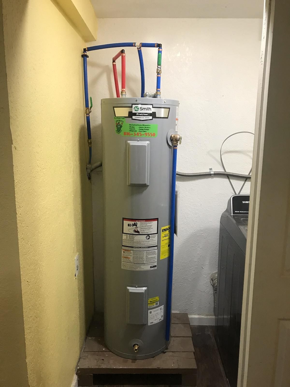 A water heater is sitting in a room next to a washer and dryer.