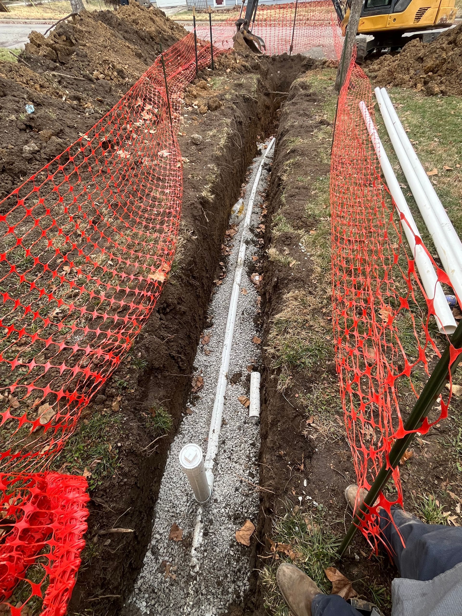 A person is laying in the dirt next to a pipe in a trench.