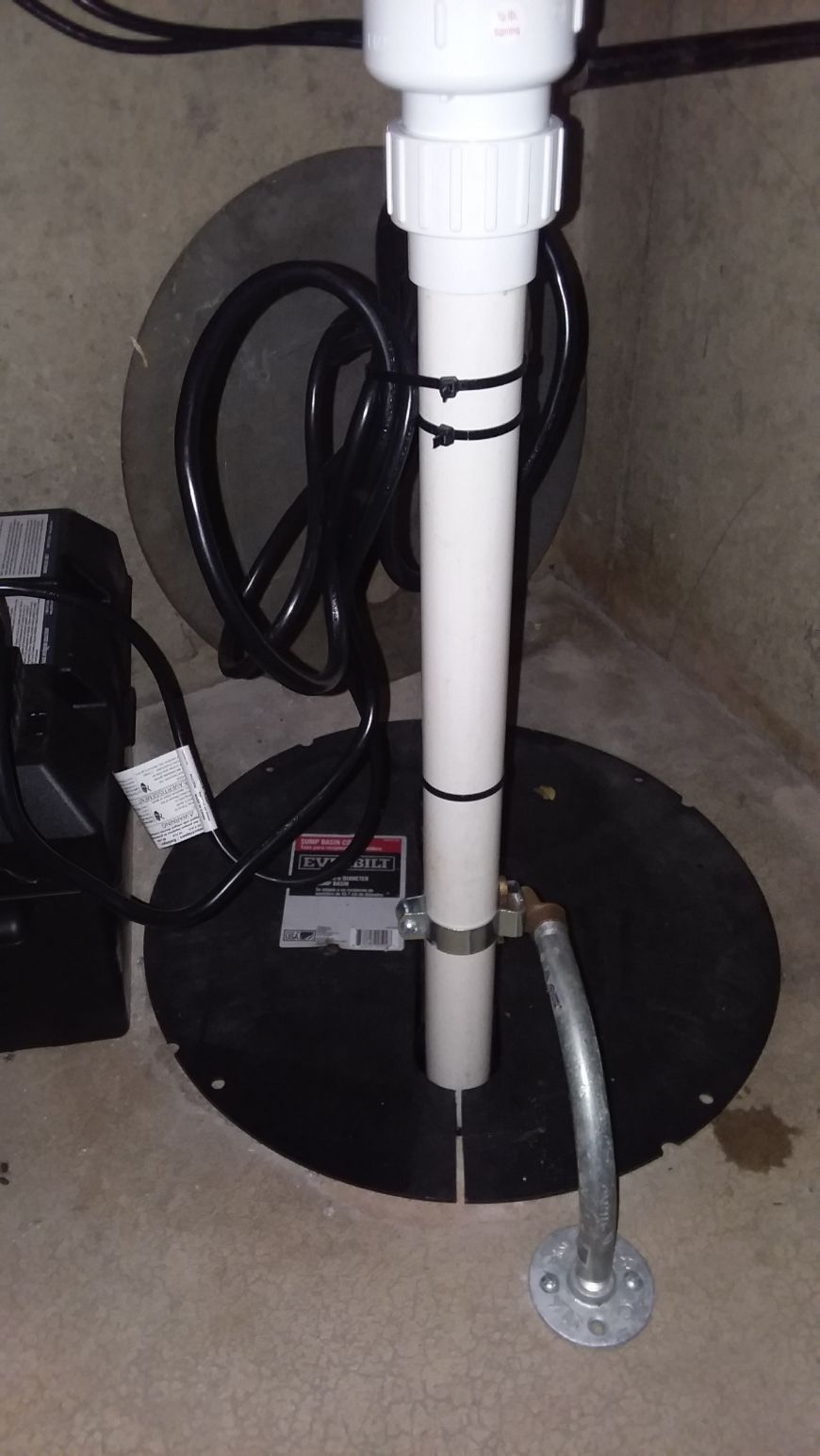 A white pipe is sitting on top of a black basement drain.