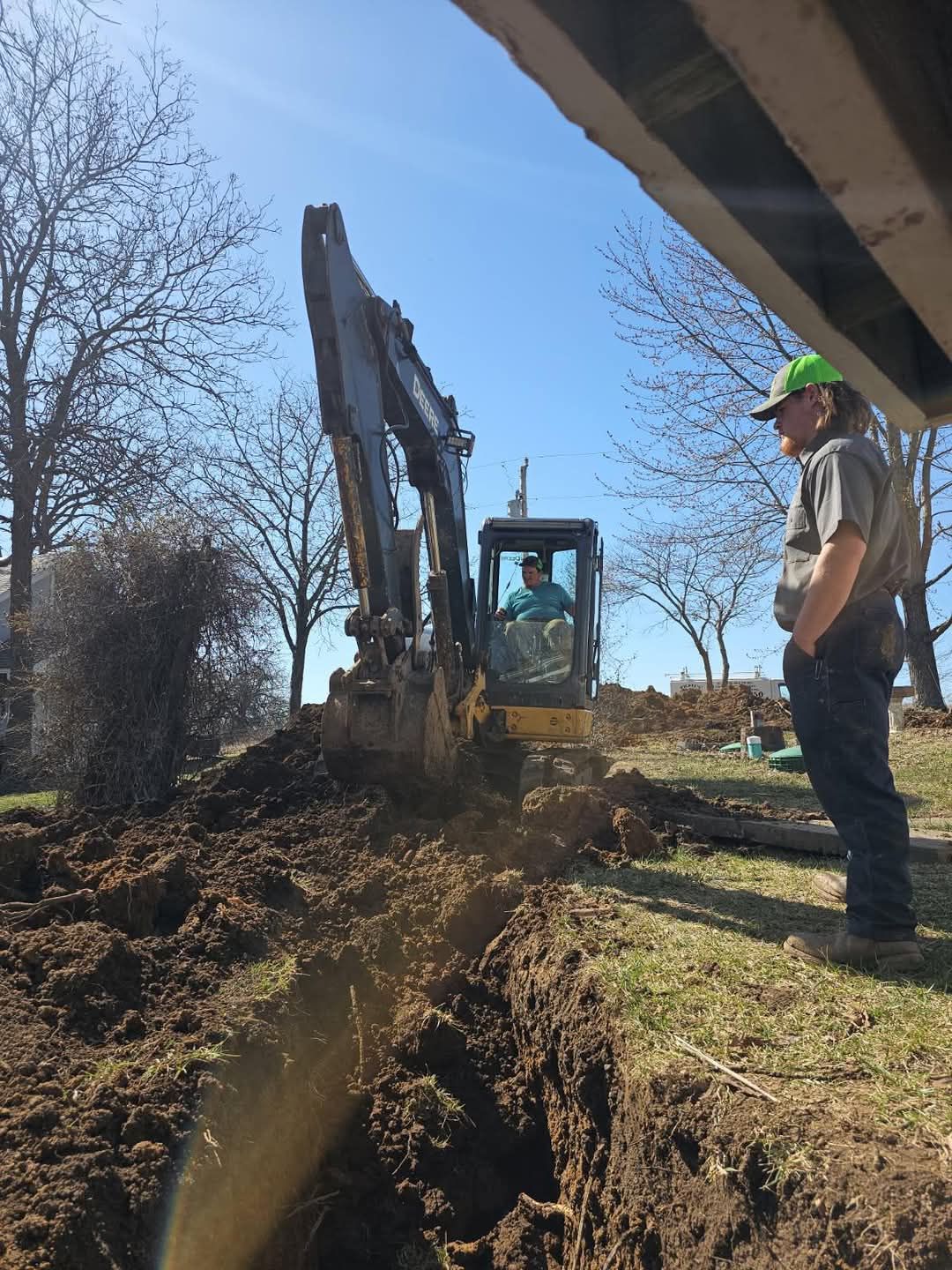 A man is standing next to an excavator in a dirt field.