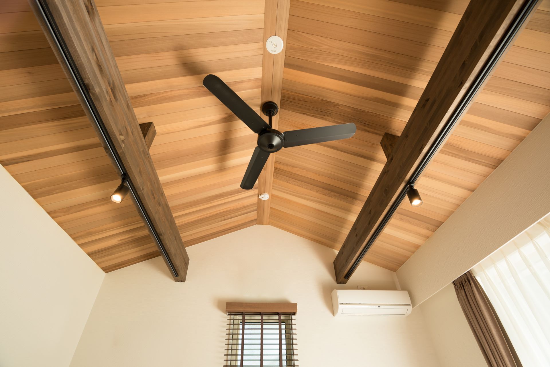 Wooden ceiling with dark beams, black fan, recessed lighting, and a small window.