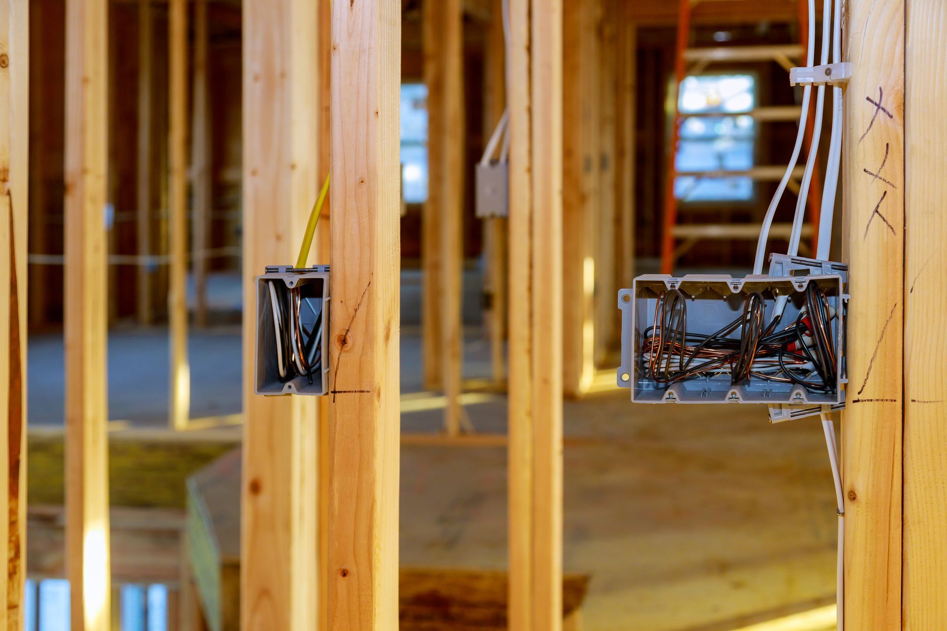 Wooden framing with exposed electrical wiring and outlet boxes in a house under construction.