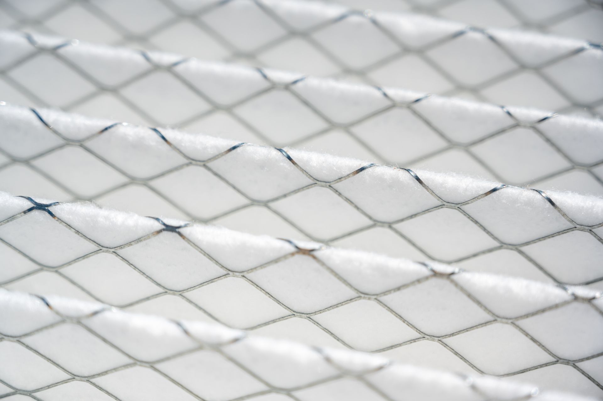 Close-up of a white, pleated HVAC air filter with a silver wire grid overlay.
