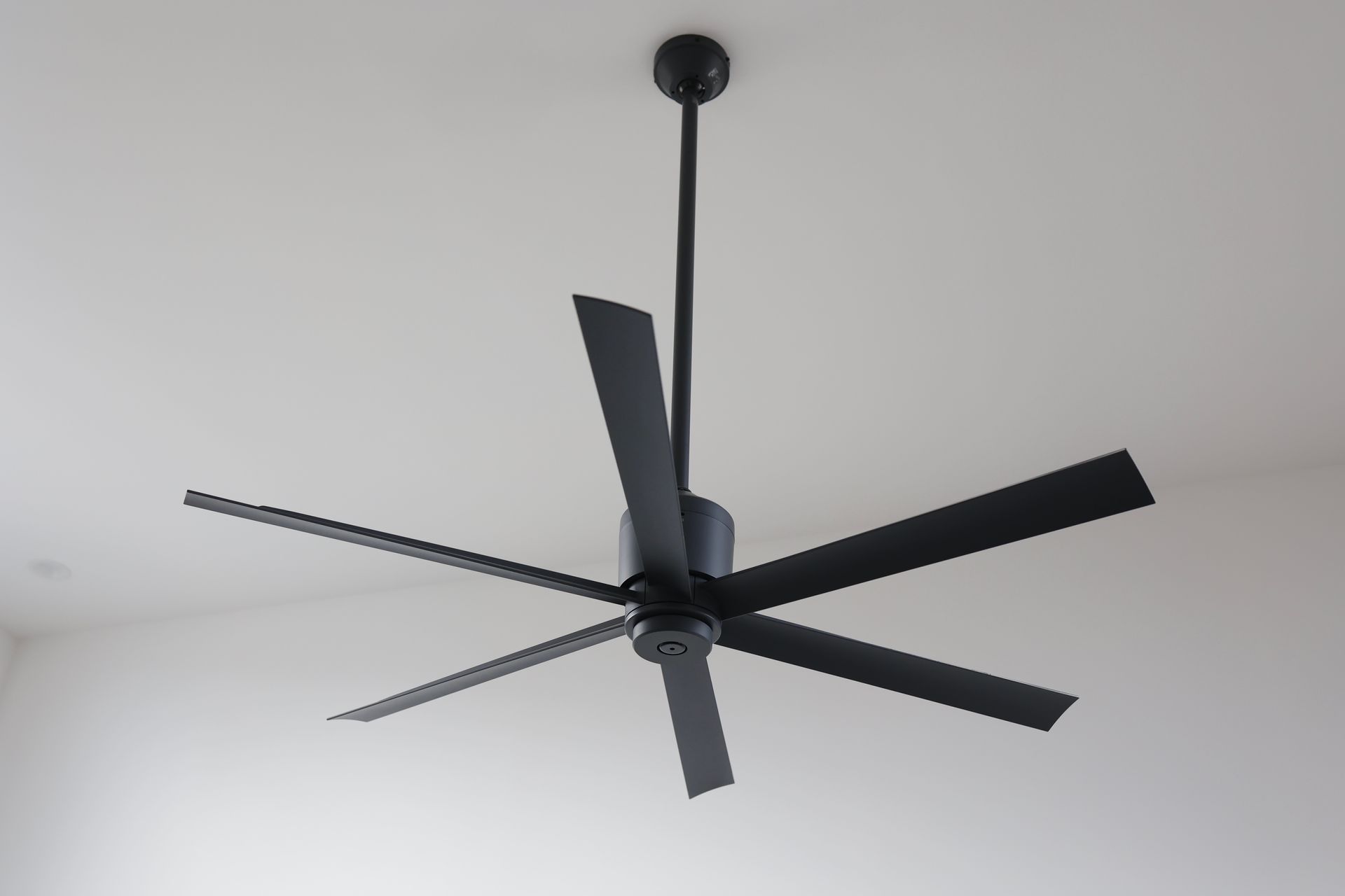 Black ceiling fan with six blades suspended from a white ceiling.
