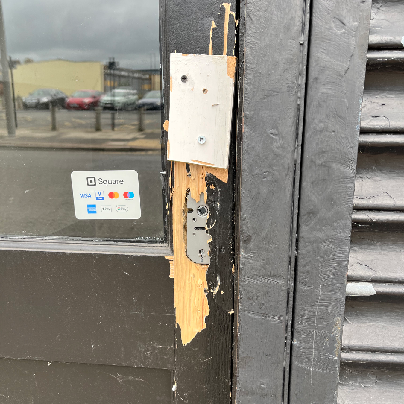 Damaged black doorframe with broken lock and a metal plate.