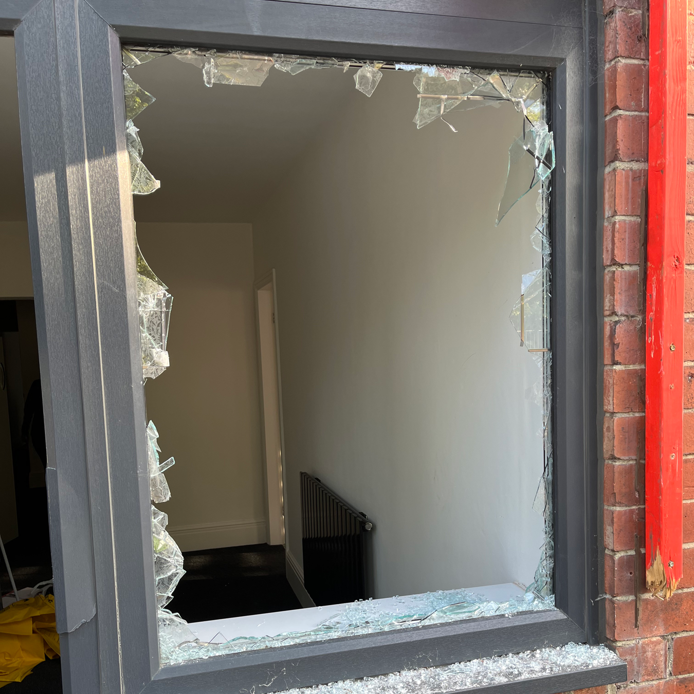 Broken window in a gray frame, exposing interior stairs. Shattered glass edges, brick exterior.