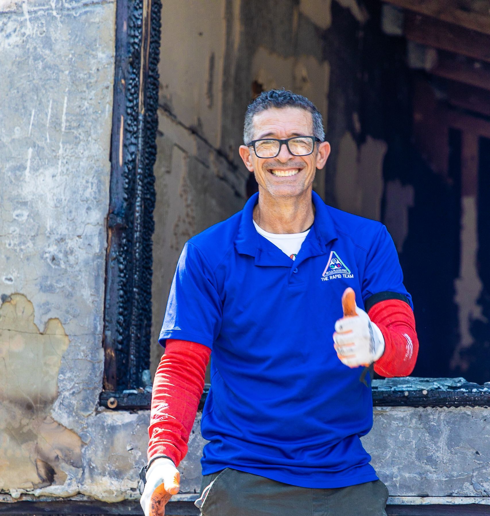 A man wearing glasses and a blue shirt giving a thumbs up