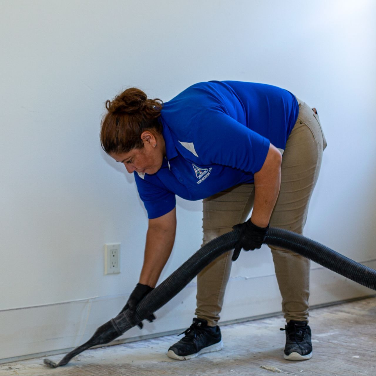 A woman in a blue shirt is vacuuming the floor