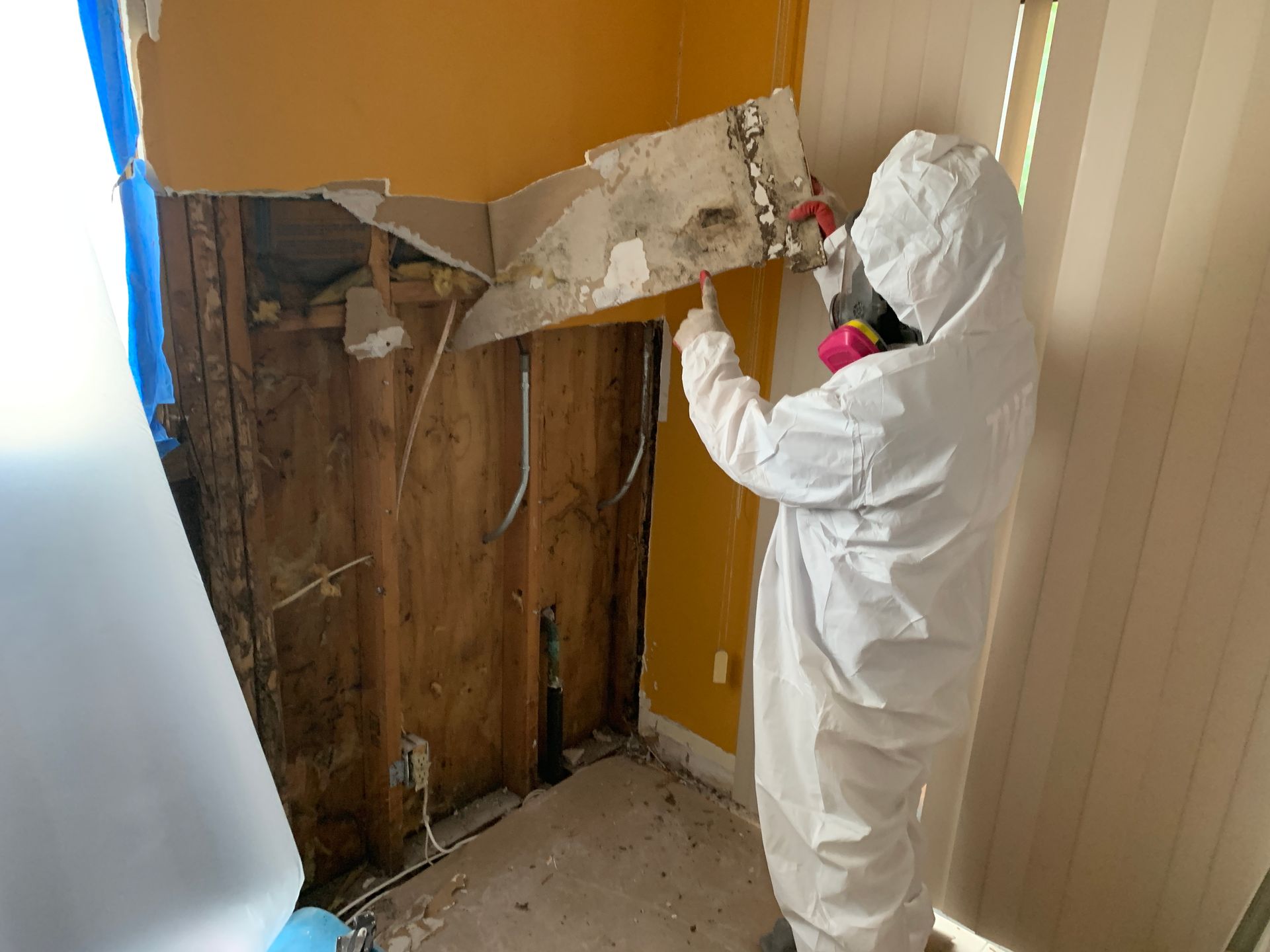 A person in a protective suit is working on a wall.