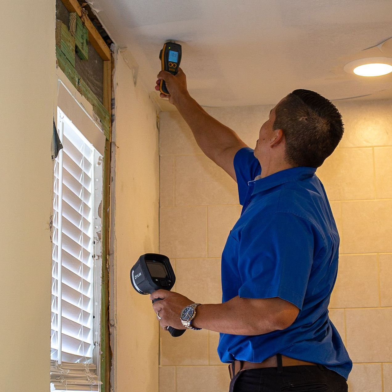 A man in a blue shirt is measuring the ceiling