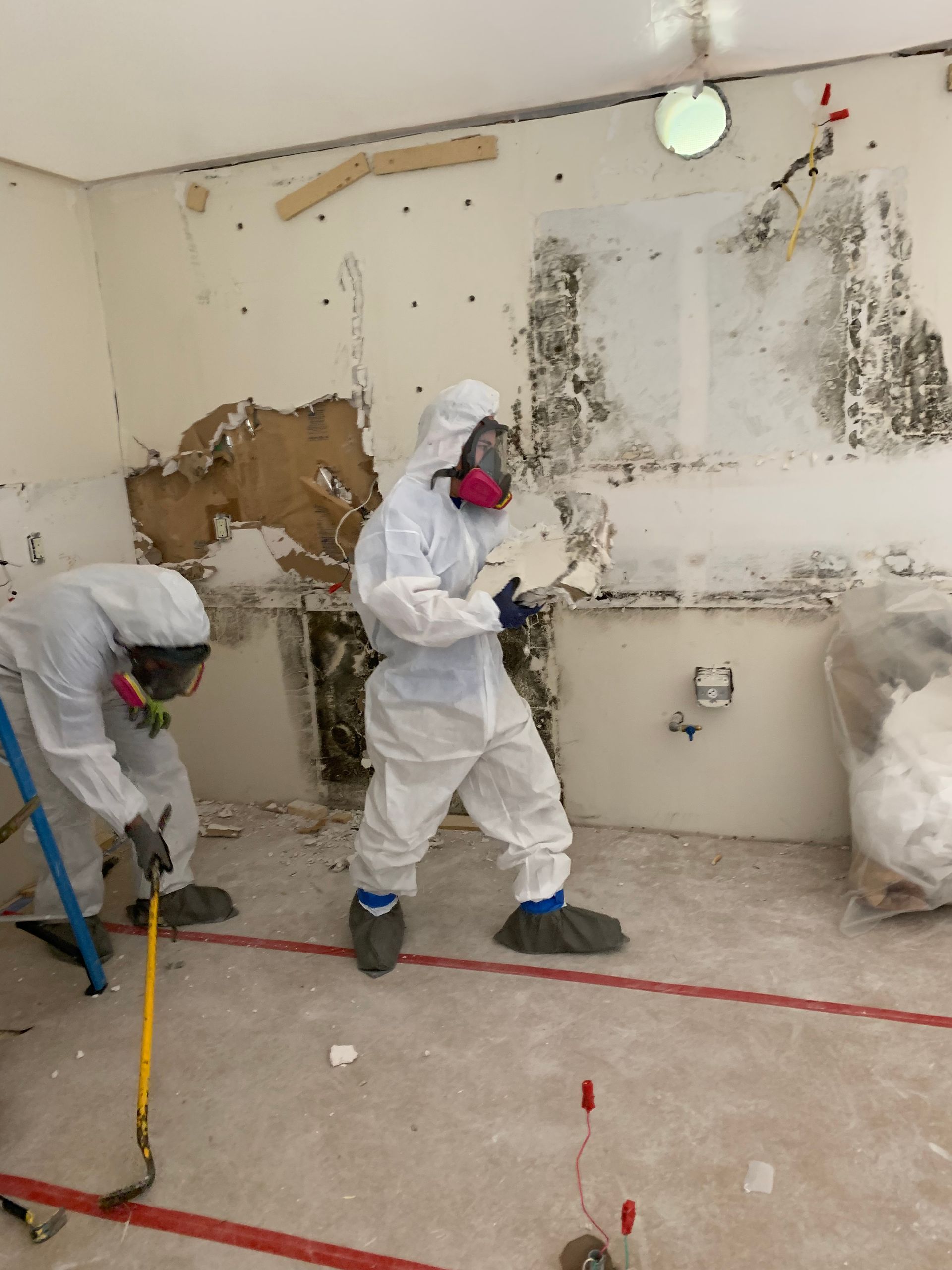 Two men in protective suits are working in a room.