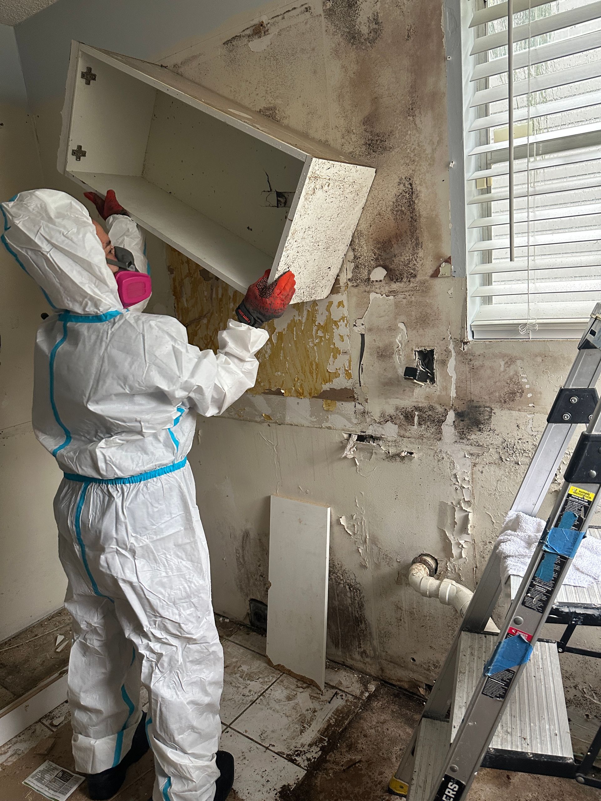 A person in a protective suit is removing a cabinet in a bathroom.