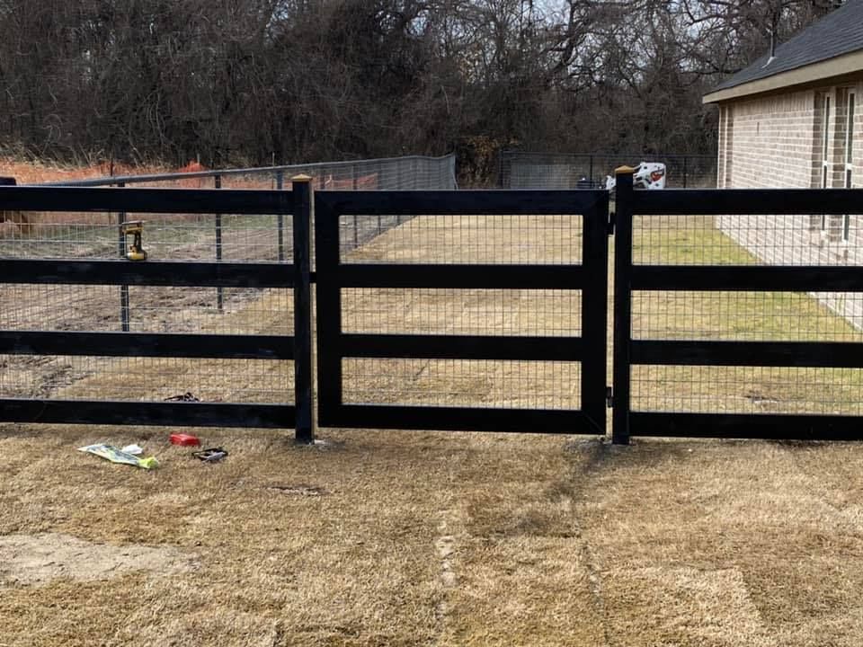 A black fence with a gate in the middle of a dirt field.