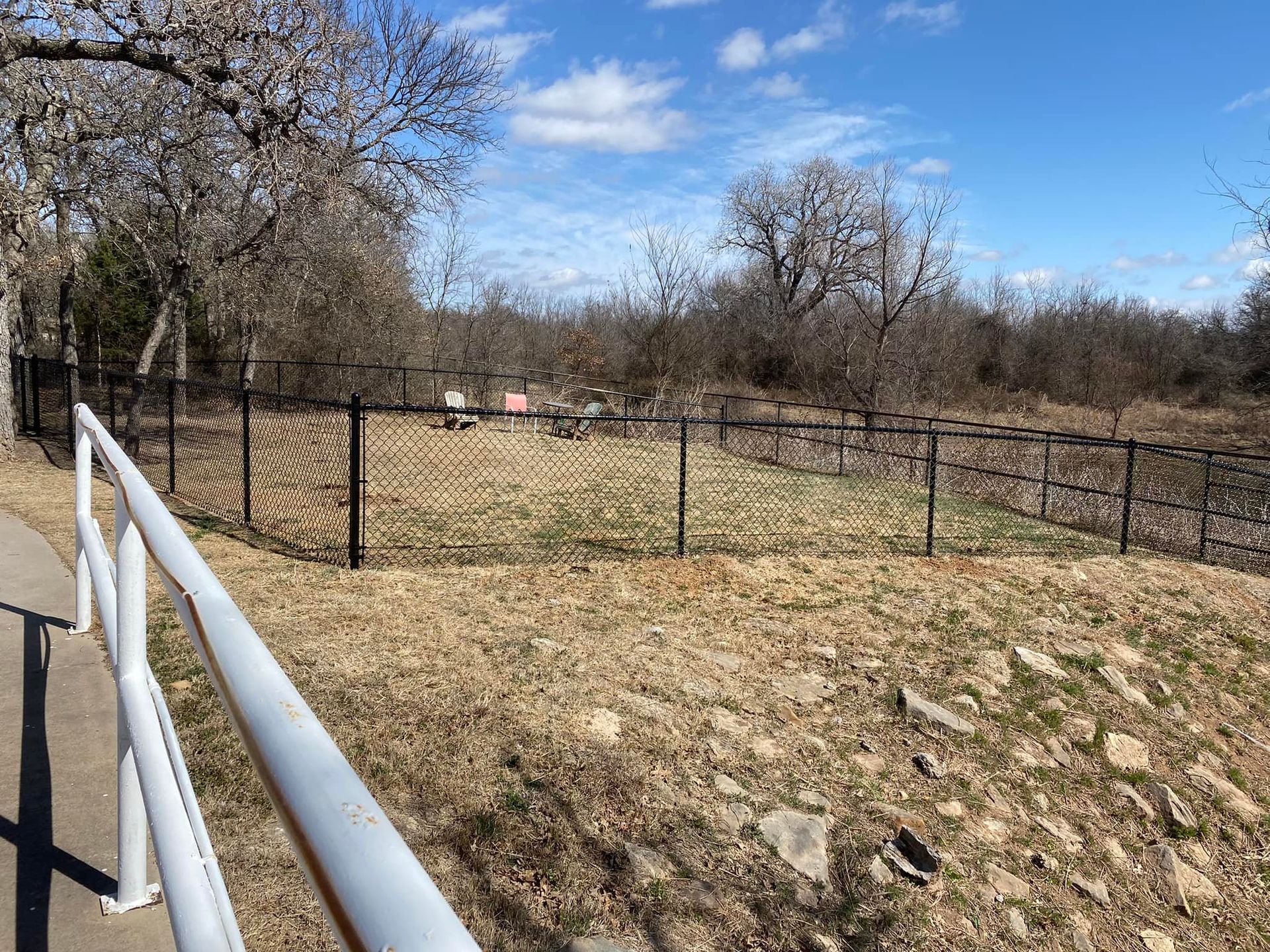 A white railing leading to a fenced in area with trees in the background.