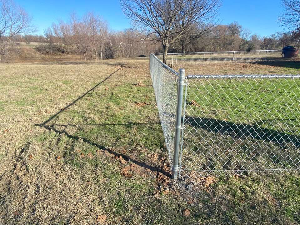 A chain link fence is surrounding a grassy field.