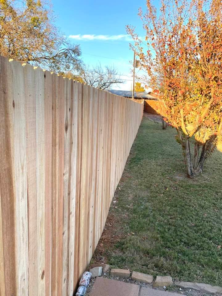 A wooden fence is surrounded by grass and trees in a backyard.