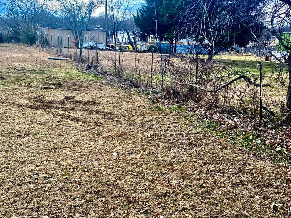 A dirt field with a fence and trees in the background.