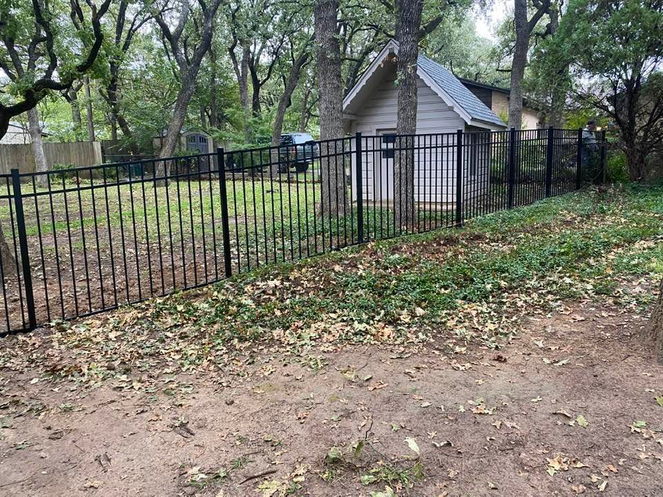 A black fence surrounds a yard with a shed in the background.