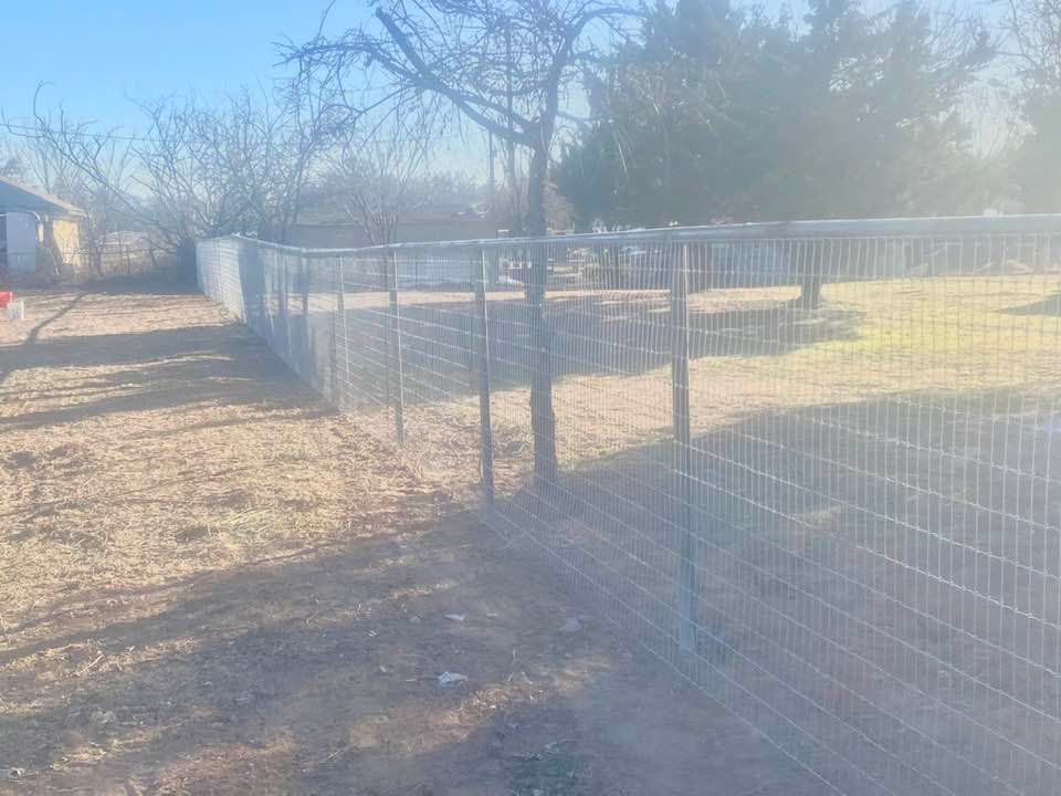 A wire fence is surrounding a yard with a house in the background.