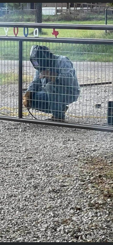 A man is welding a fence in a gravel area.