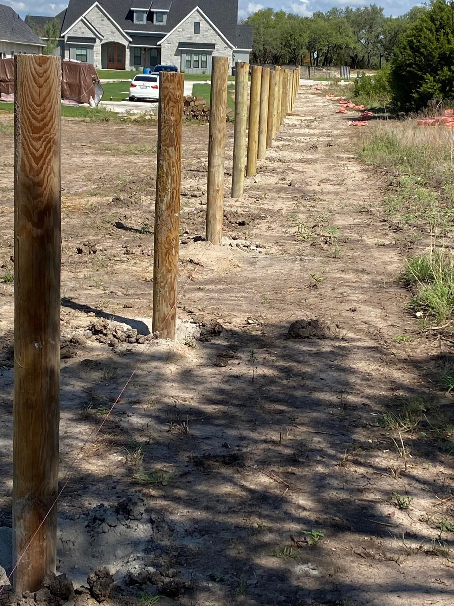 A wooden fence is being built in a dirt field with a house in the background.