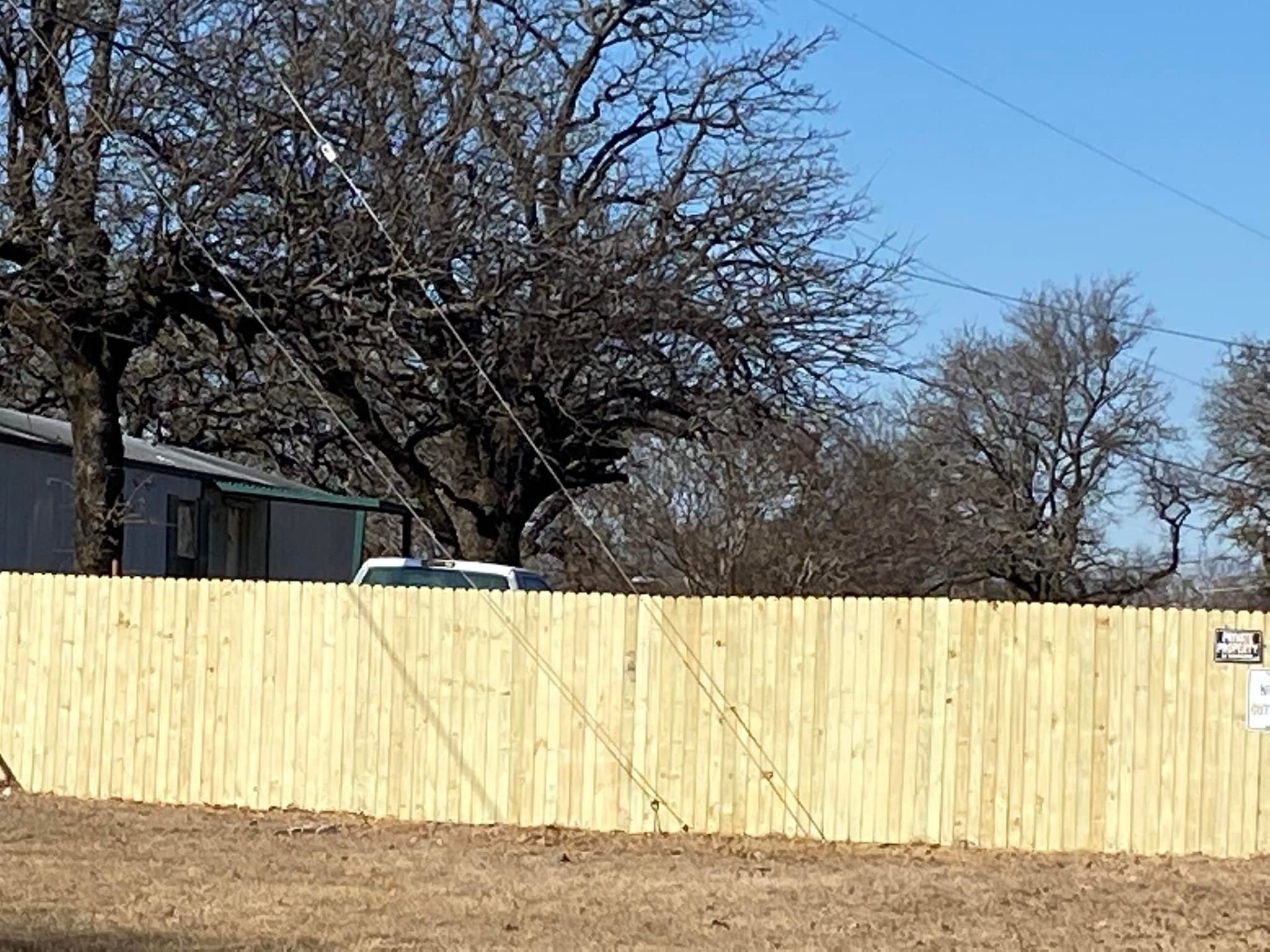 A wooden fence surrounds a dirt field with trees in the background.