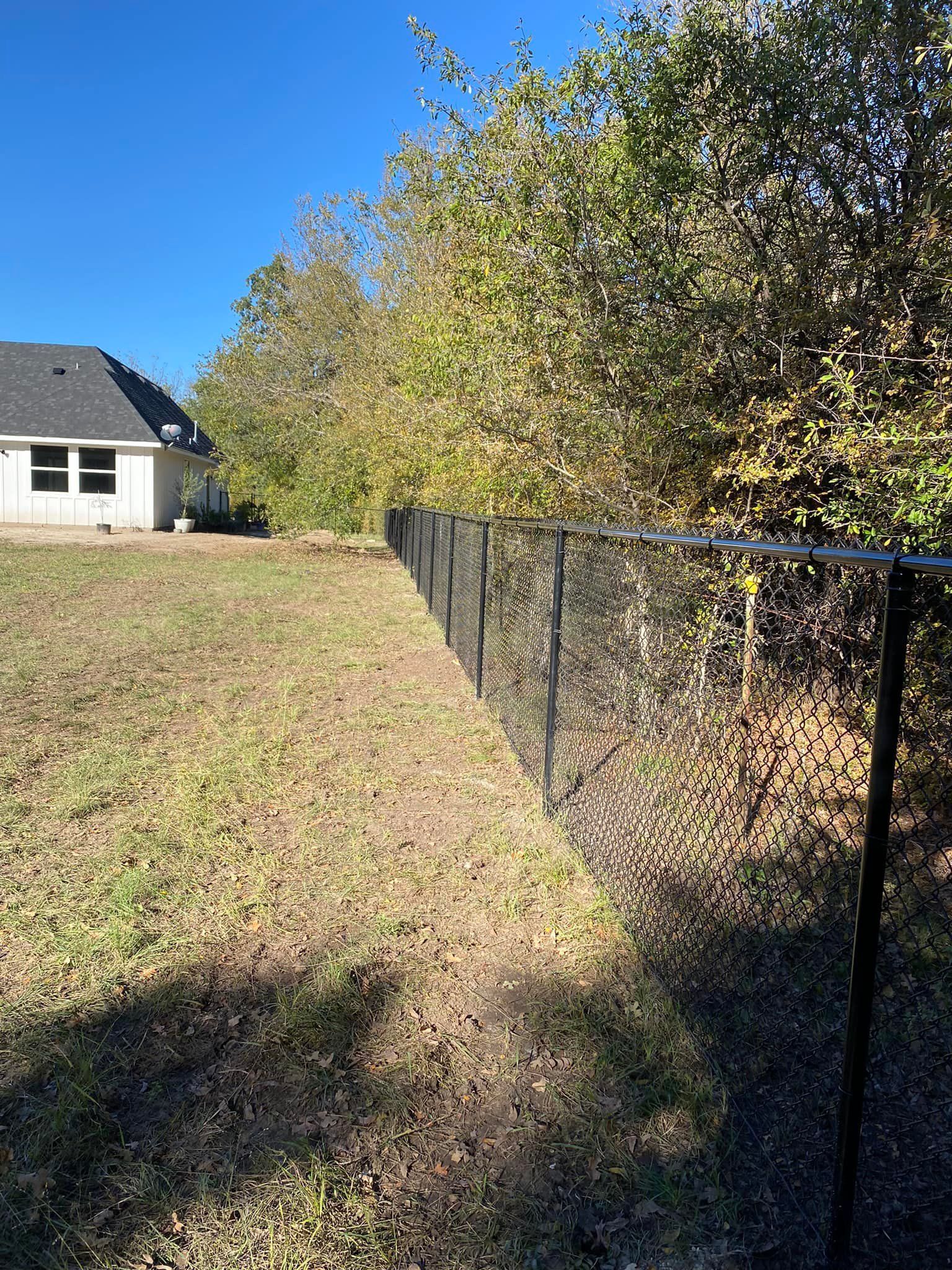 A chain link fence surrounds a lush green field in front of a house.