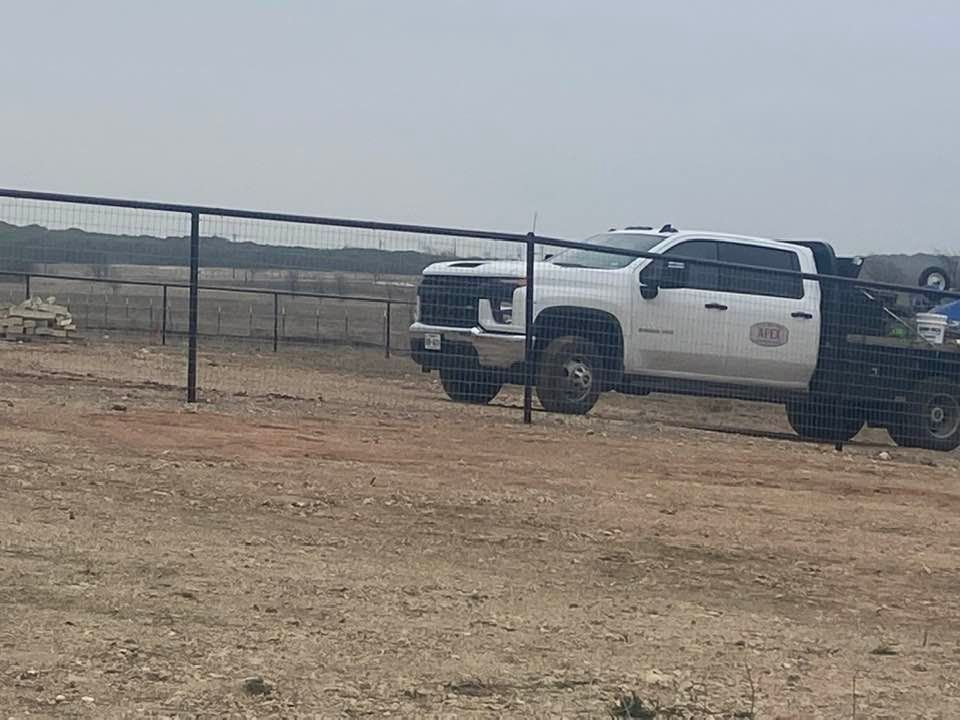 A white truck is parked in a dirt field next to a fence.