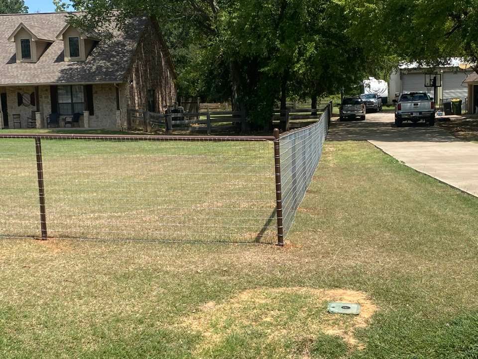 A fence is surrounding a grassy field in front of a house.