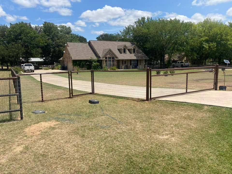 A fence surrounds a driveway leading to a house.