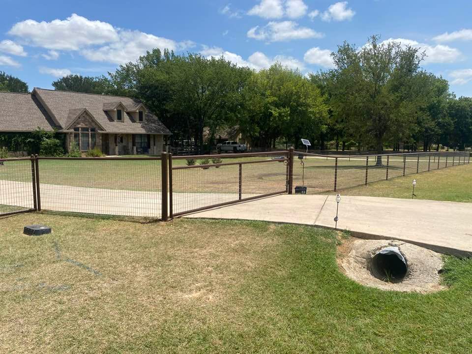 A fence surrounds a driveway in front of a house.