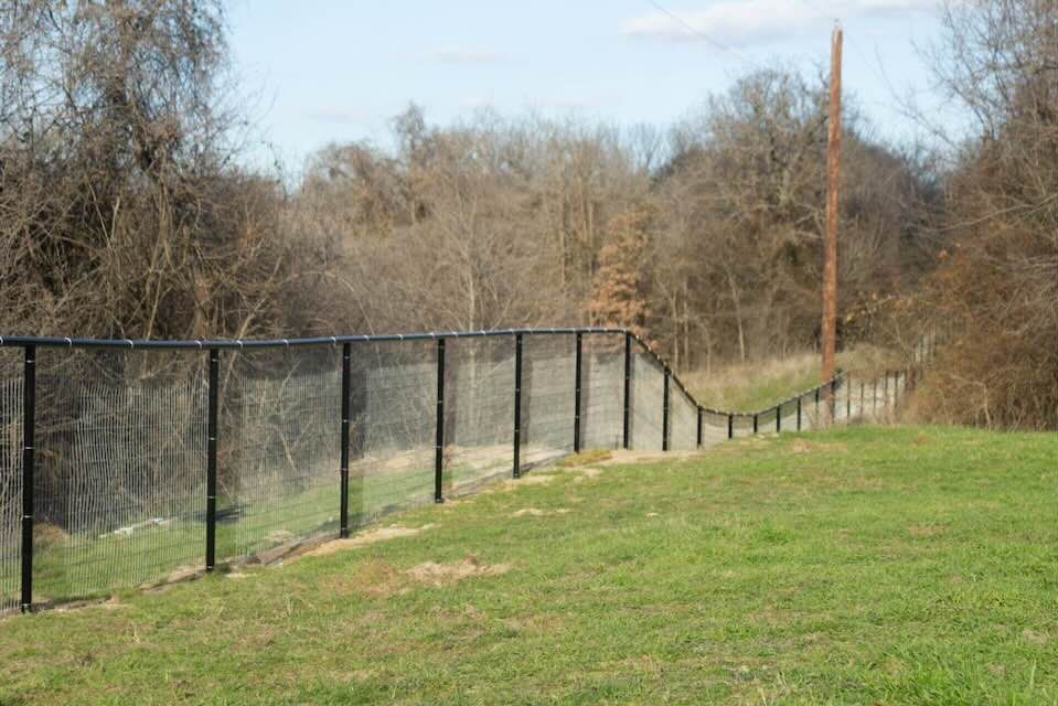 A fence surrounds a grassy field with trees in the background.