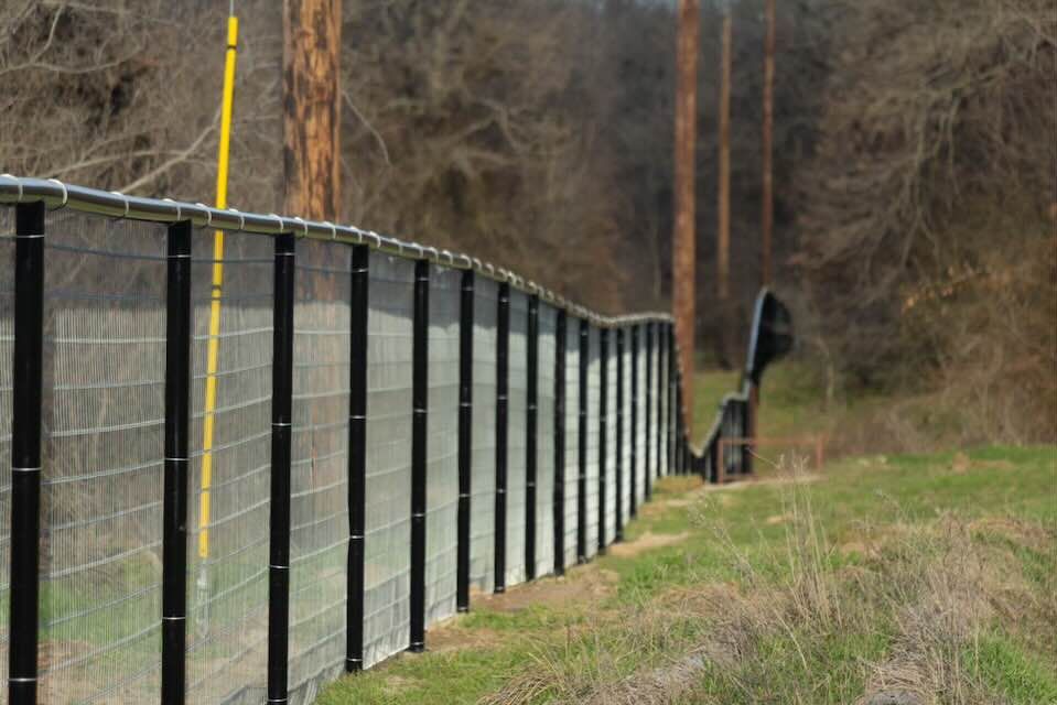 A fence surrounds a grassy field with telephone poles in the background.