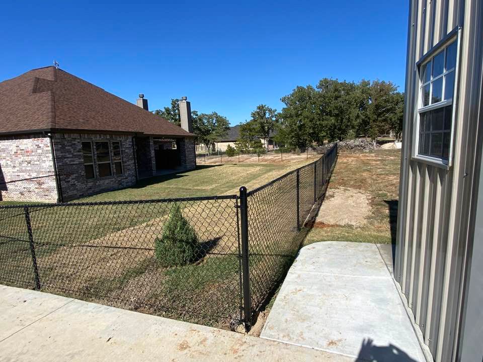 A chain link fence is surrounding a yard next to a house.