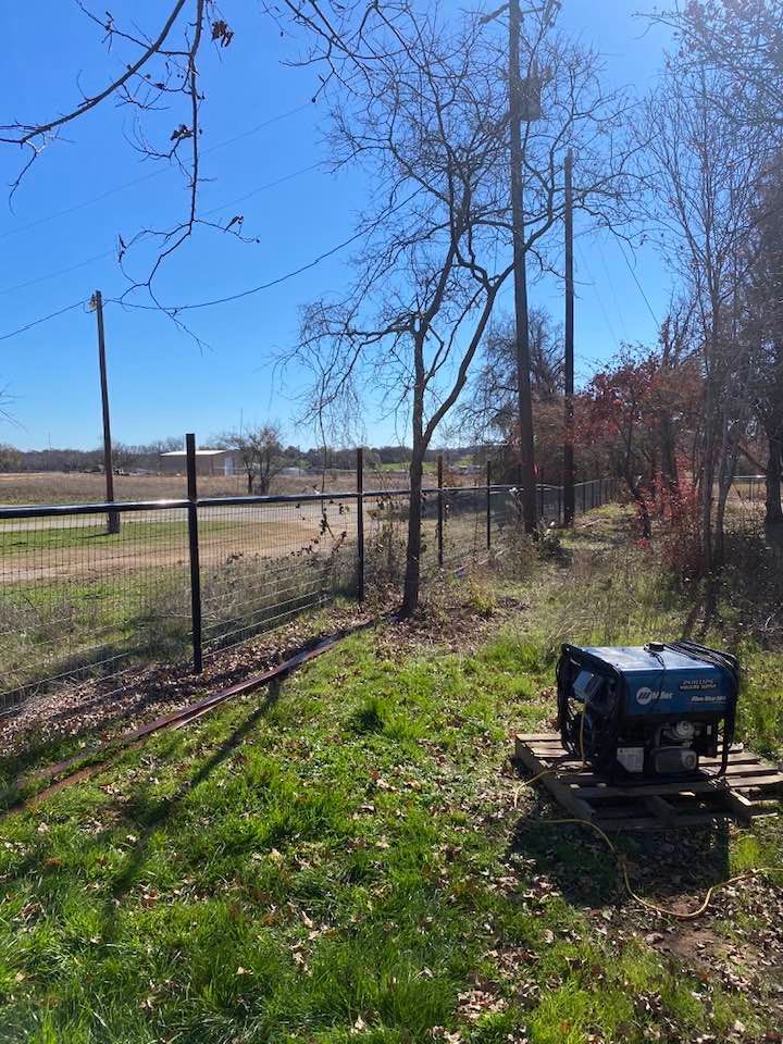 A generator is sitting in the middle of a grassy field next to a fence.